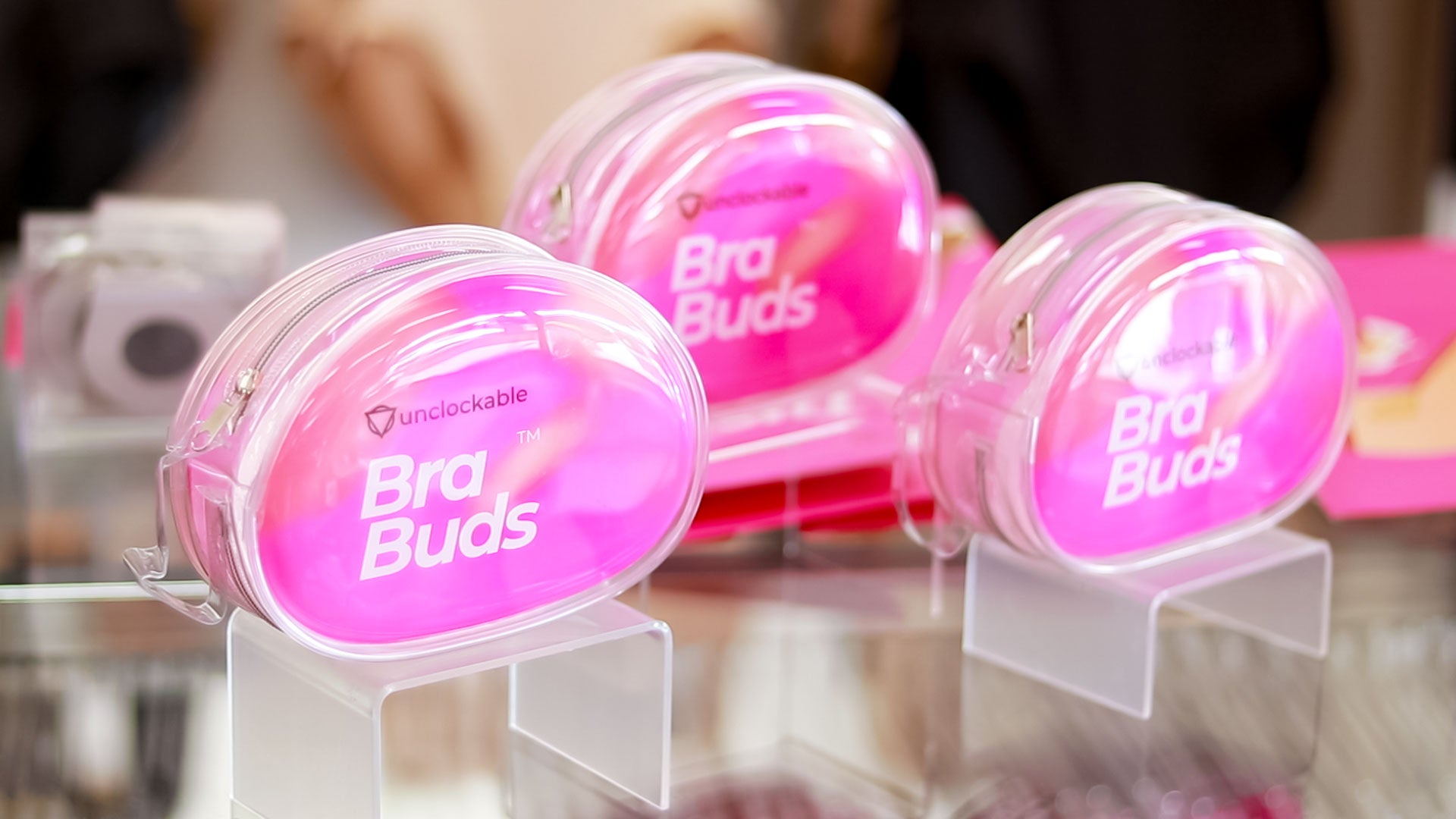 Pink transparent oval-shaped case with ’bra buds’ branding and the ’unlockable’ logo.