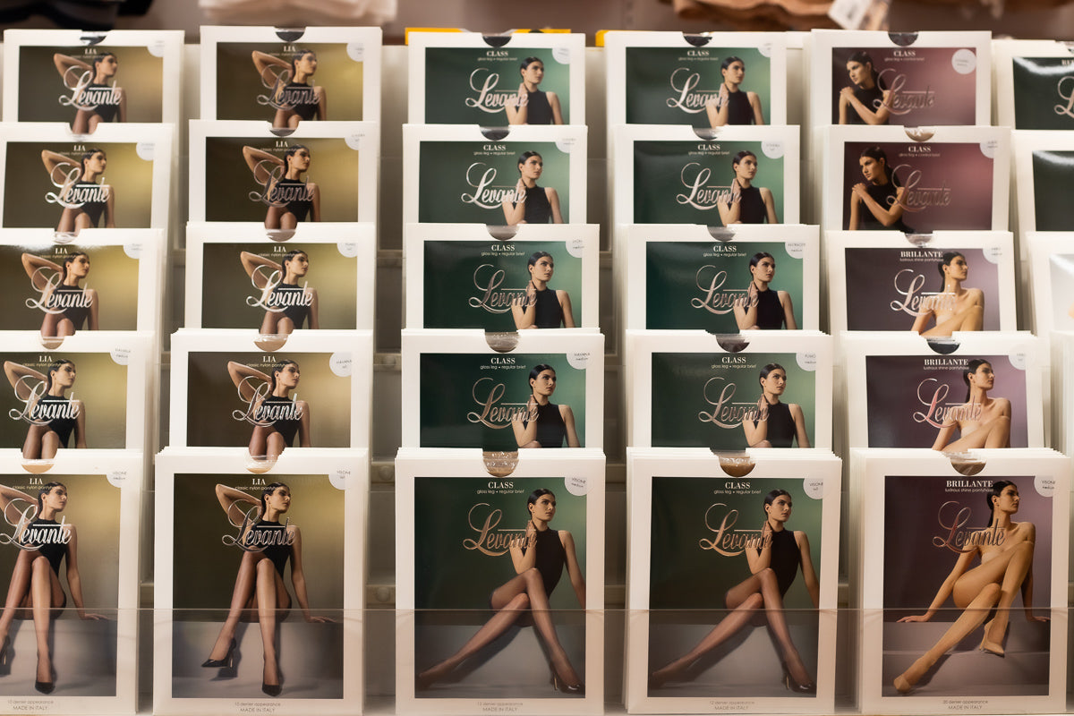 White rectangular boxes of Levante brand hosiery, featuring elegant packaging with images of models in black hosiery against muted green and purple backgrounds.