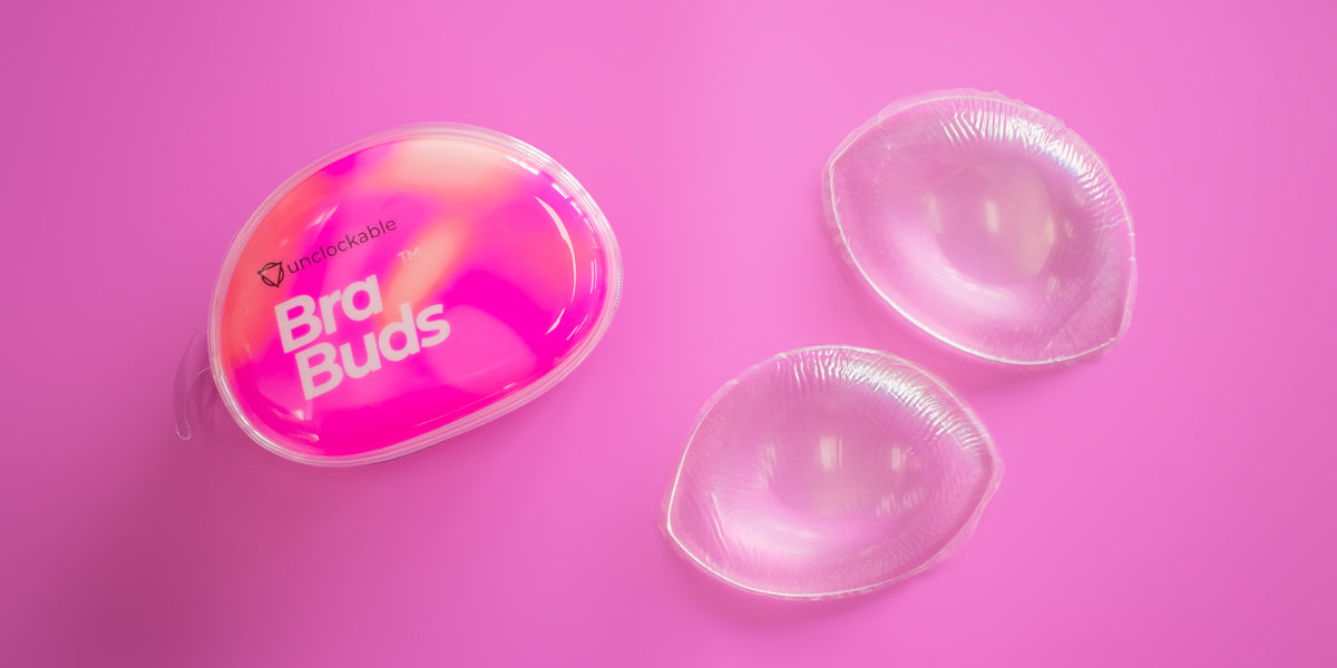 a pair of silicone breast forms next to their packaging on a solid pink background