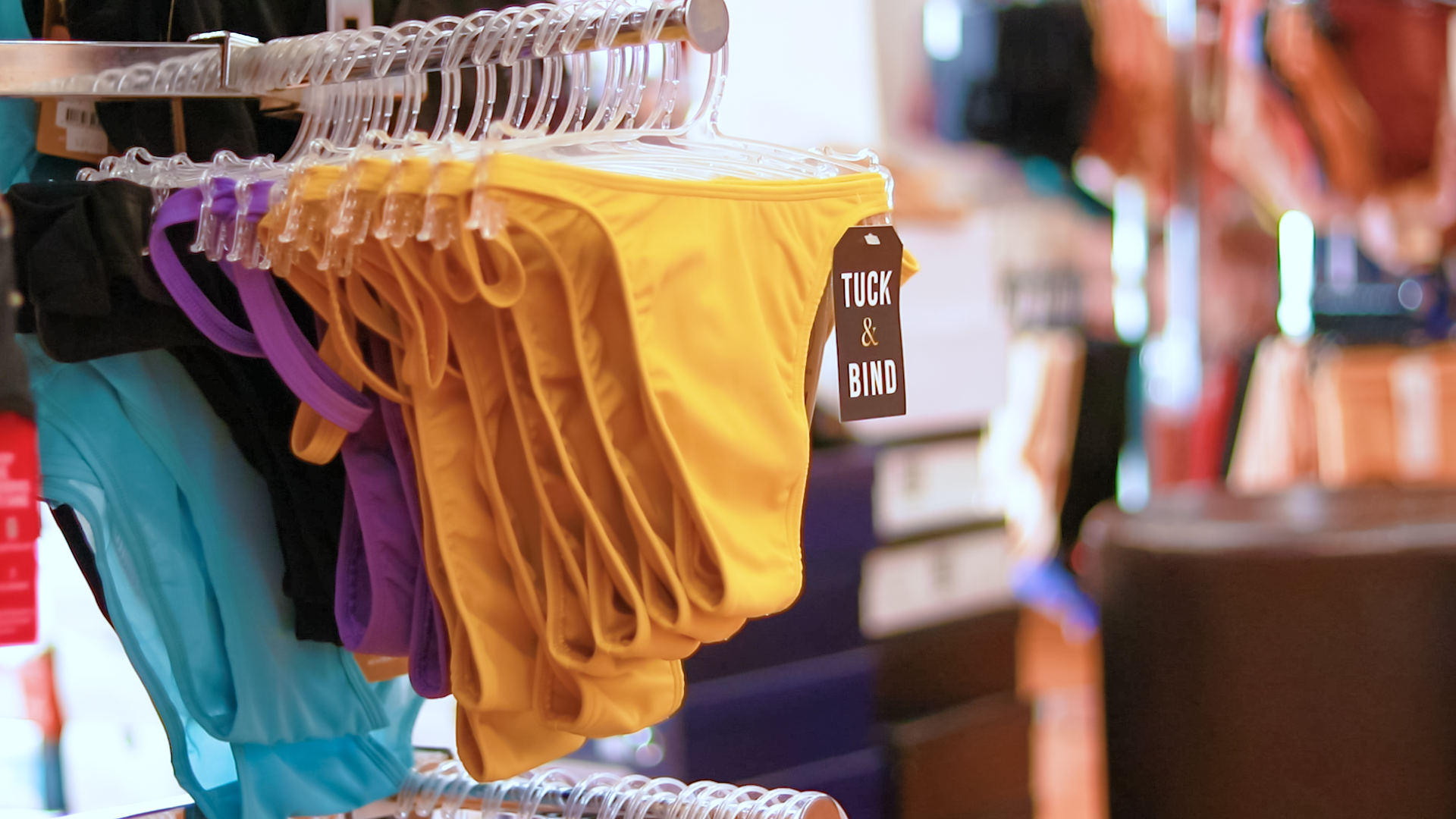 Yellow tucking underwear hanging on a rack, featuring a smooth fabric and a simple design with a black tag that reads ’tuck & bind.’