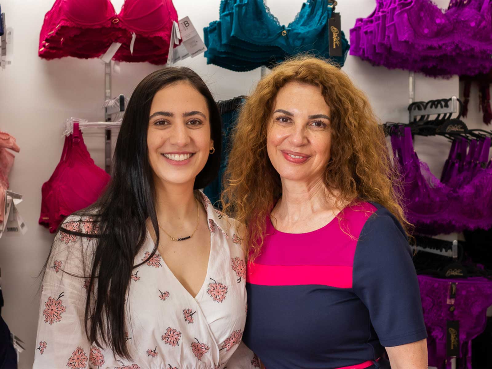 Two breast form fitters smiling in from of wall of underwear