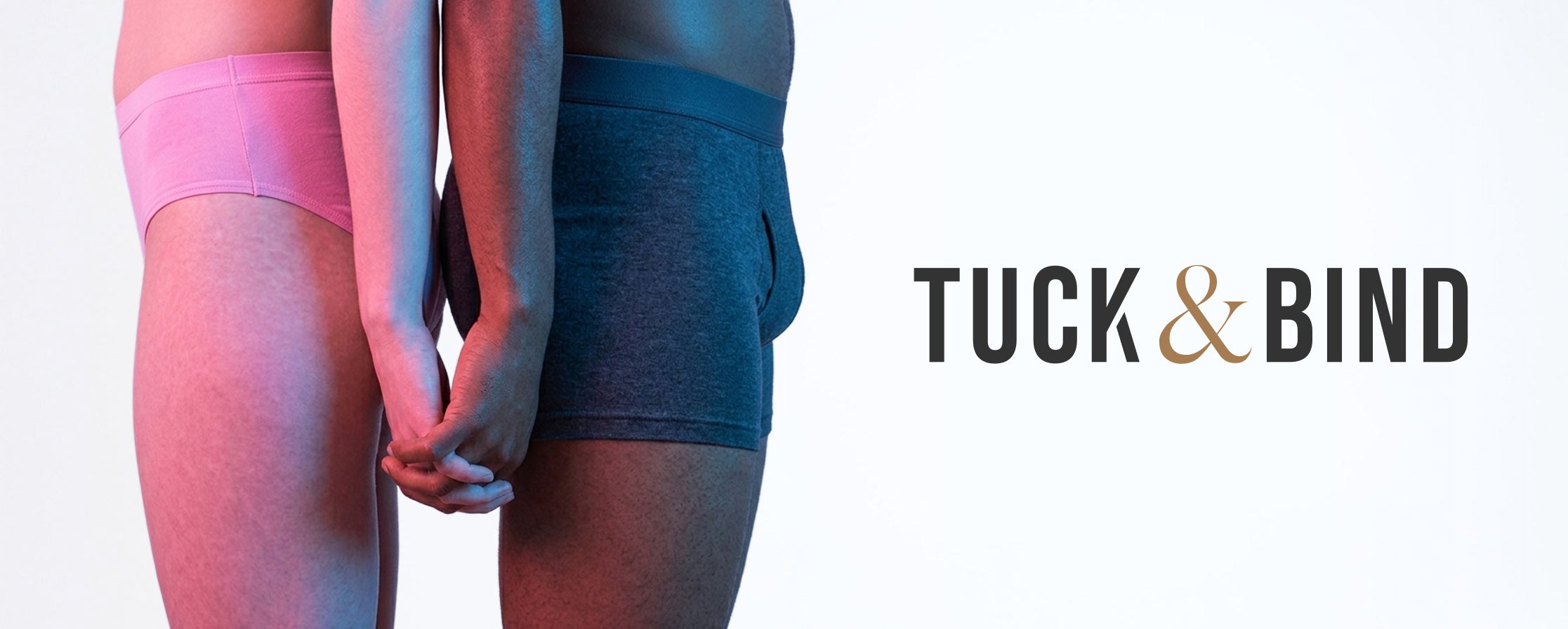 Two people holding hands with pink and blue transgender lighting on them. The person on the left is wearing a pink tucking gaff, the person on the right wears dark blue packing underwear. The "Tuck & Bind" logo is on the right.