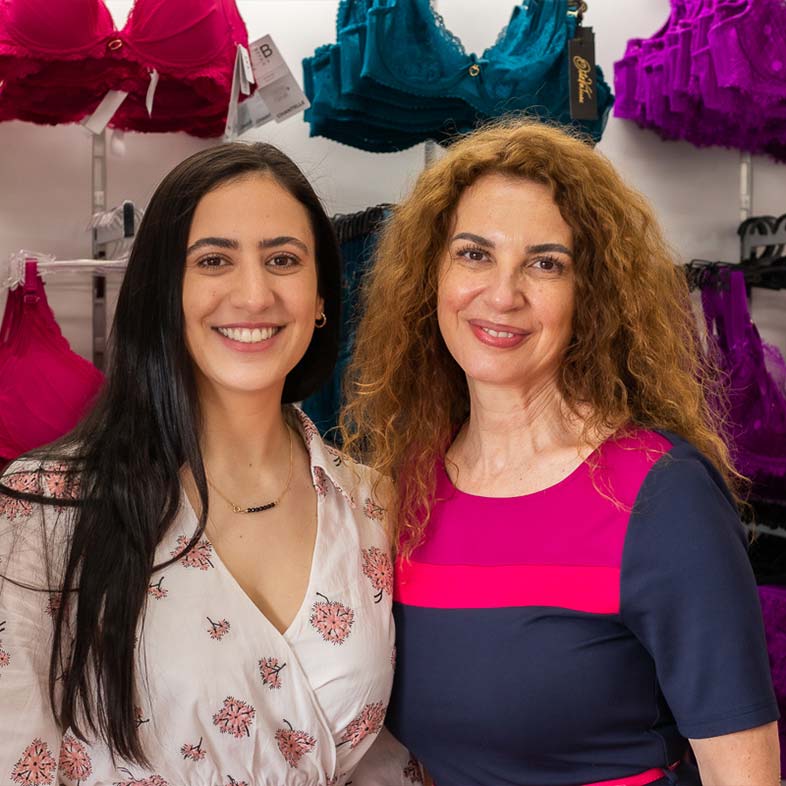 Two bra fitters standing in front of wall of bras